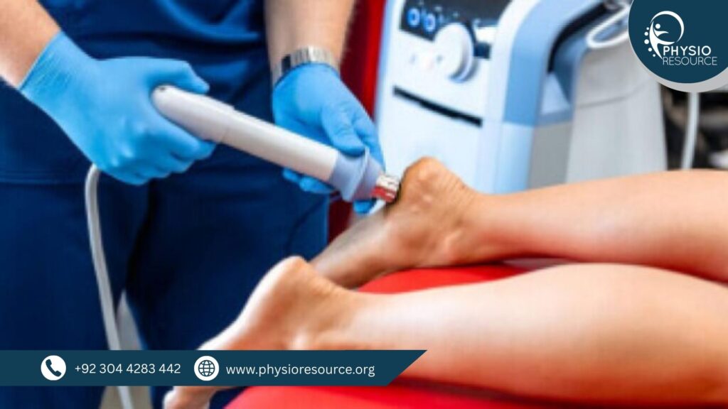 Pakistani physiotherapist using a handheld shockwave therapy device on a patient’s foot or ankle. The patient lies on a red treatment table in a clinical setting, with a medical control unit visible in the background.