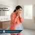 Pakistani woman in modest clothing sneezing and experiencing urine leakage discomfort at home – Physio Resource