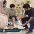 Male pediatric physiotherapist checking a boy’s ankle-foot brace while his mother sits beside him.