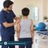 Male physiotherapist assessing a child’s shoulder alignment during a scoliosis assessment.