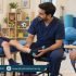 Male pediatric physiotherapist supporting a boy’s lower leg during an assessment while his father watches.