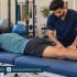 Male physiotherapist examining the back of an athlete’s thigh while the athlete lies face down on a treatment couch.